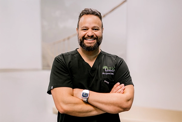 Chiropractor Cyrus Laali Smiling In Black Polo In Front Of Blurred Background